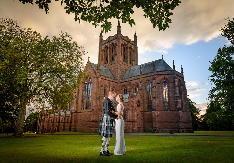 Bride and groom pose together outside The Crichton Memorial Church in Dumfries